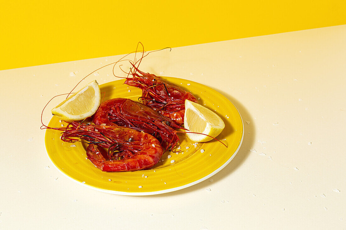 Tasty seafood of cooked red shrimps with fresh lemon slices and coarse salt on two color background
