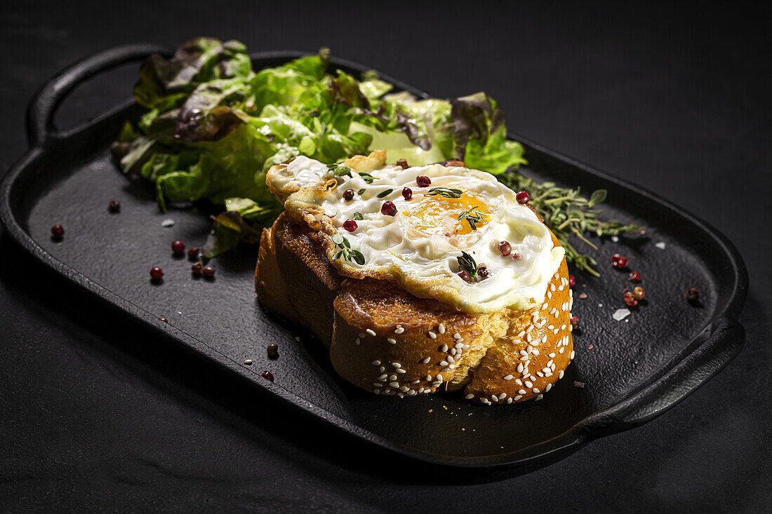 Fried egg on brioche served on tray with fresh lettuce for appetizing breakfast on black background