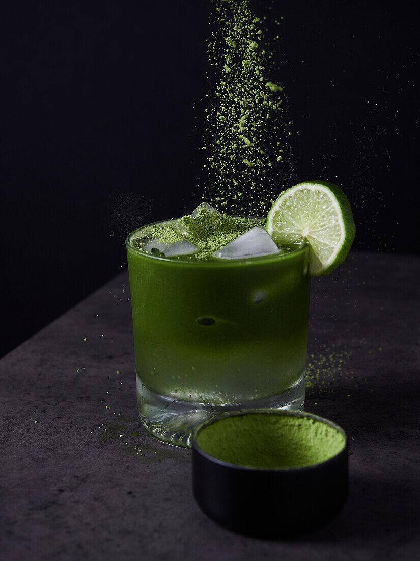 Erfrischendes Kaltgetränk mit Limette und Matcha-Pulver mit Eiswürfeln auf dunkler Oberfläche