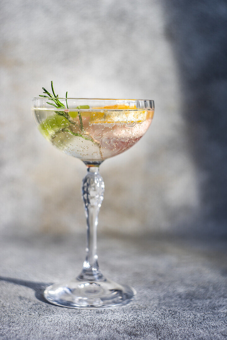 Summer tropical cocktail of vodka and sprite with ripe fruits and rosemary on grey background