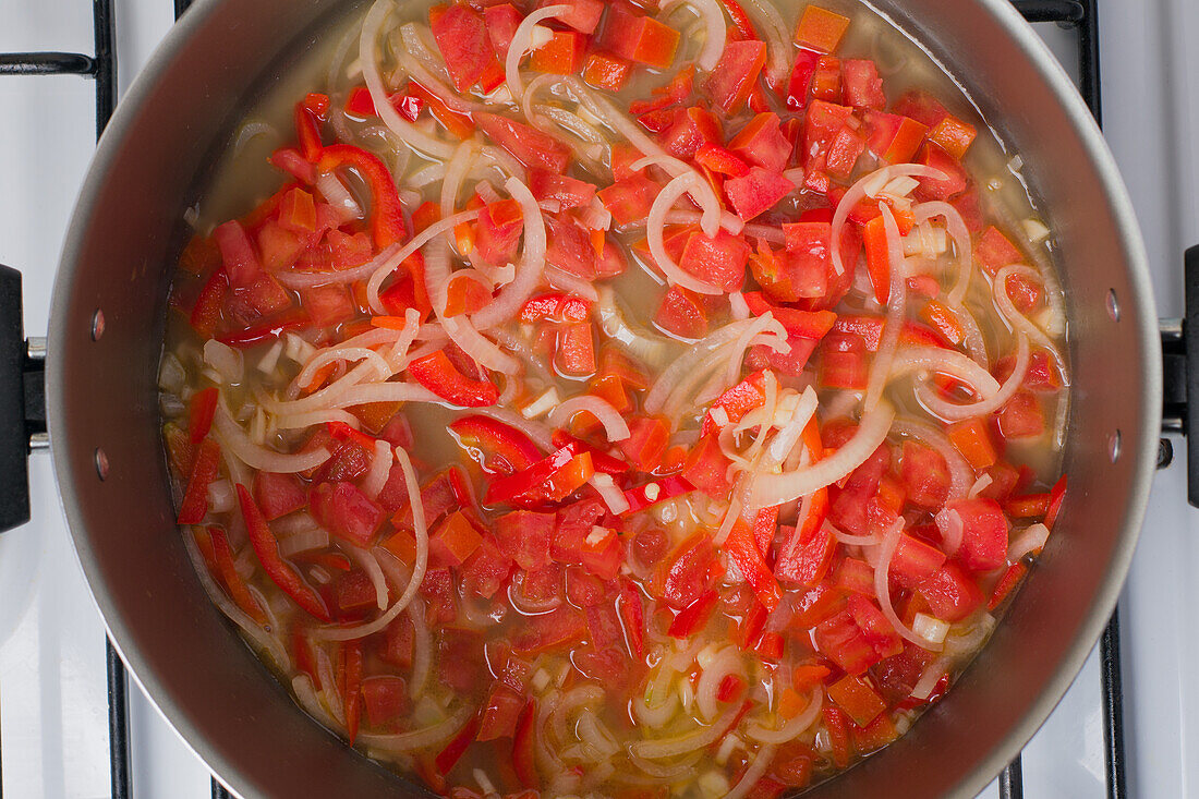 Draufsicht auf gehackte Tomaten und Zwiebeln in einem Topf, der auf dem Herd für das Mittagessen kocht