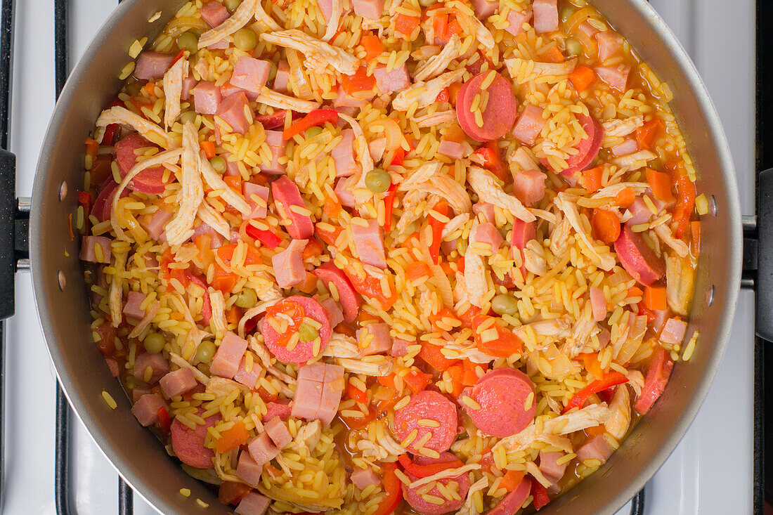 Draufsicht auf gehackte Tomaten und Zwiebeln Valenciana-Reis im Topf, der auf dem Herd für das Mittagessen kocht