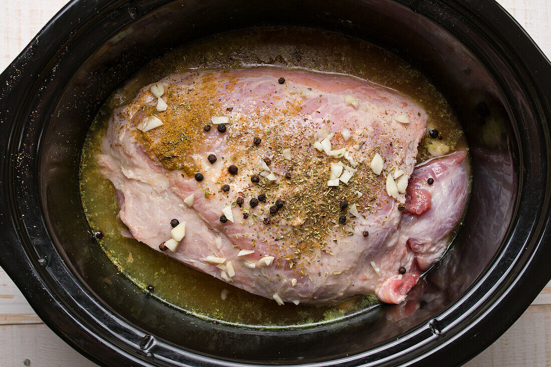 From above of tasty uncooked meat with spices and garlic seasoning with savory marinade in slow cooker