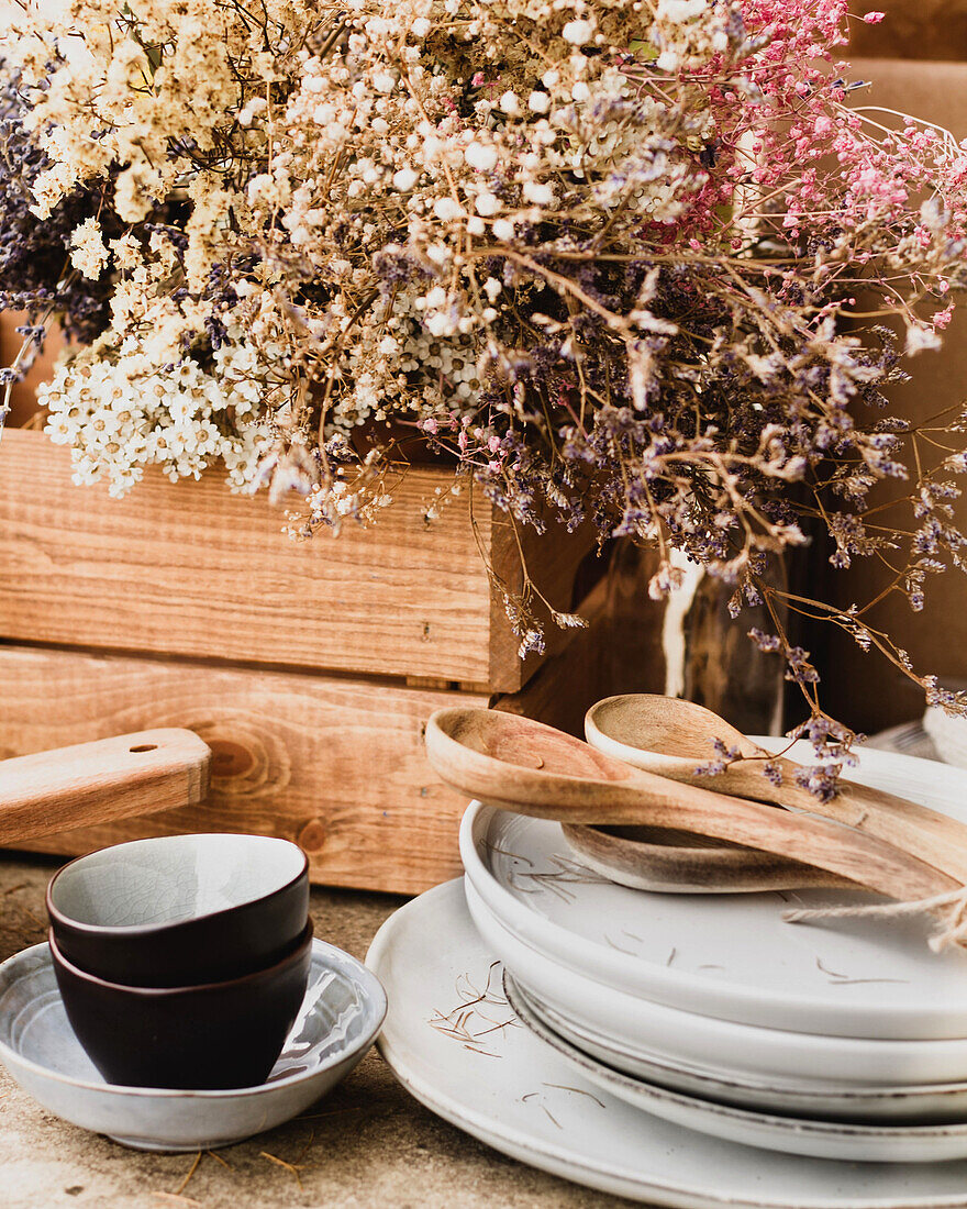 Black and white ceramic crockery with wooden spoons beside brown oak crate with lush bouquet of colorful wildflowers on table in autumn garden