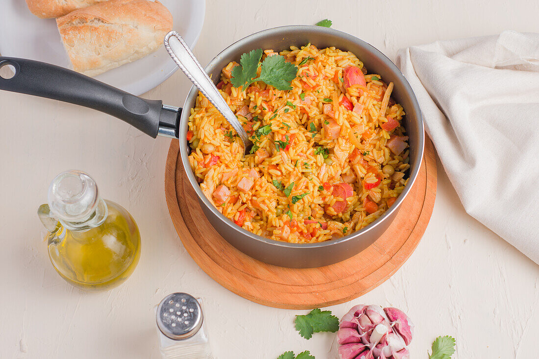 From above of saucepan with delicious rice with herbs chopped meat and vegetables on wooden stand served with oil garlic and loaf