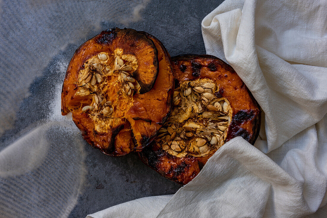 From above of tasty appetizing healthy baked pumpkin halves with seeds on gray table with kitchen cloth