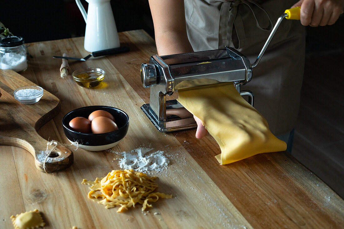 Unrecognizable person preparing raviolis and pasta at home. She is using a pasta machine