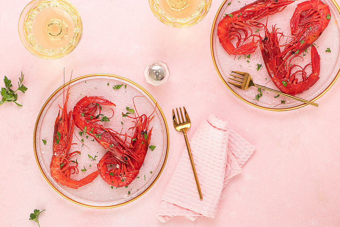 From above glass plate with tasty fried tiger shrimps placed near glass of wine on table pink background