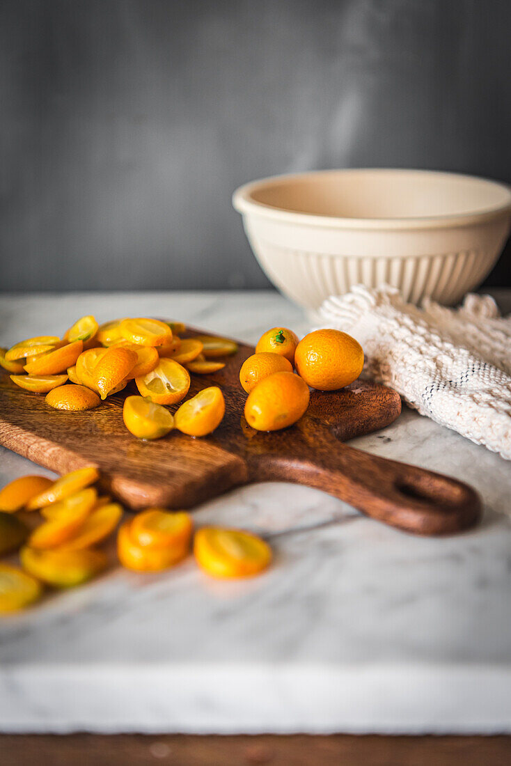 Stapel frischer, in Orangen geschnittener Kumquats auf einem hölzernen Schneidebrett auf einem Marmortisch mit Handtuch in der Küche