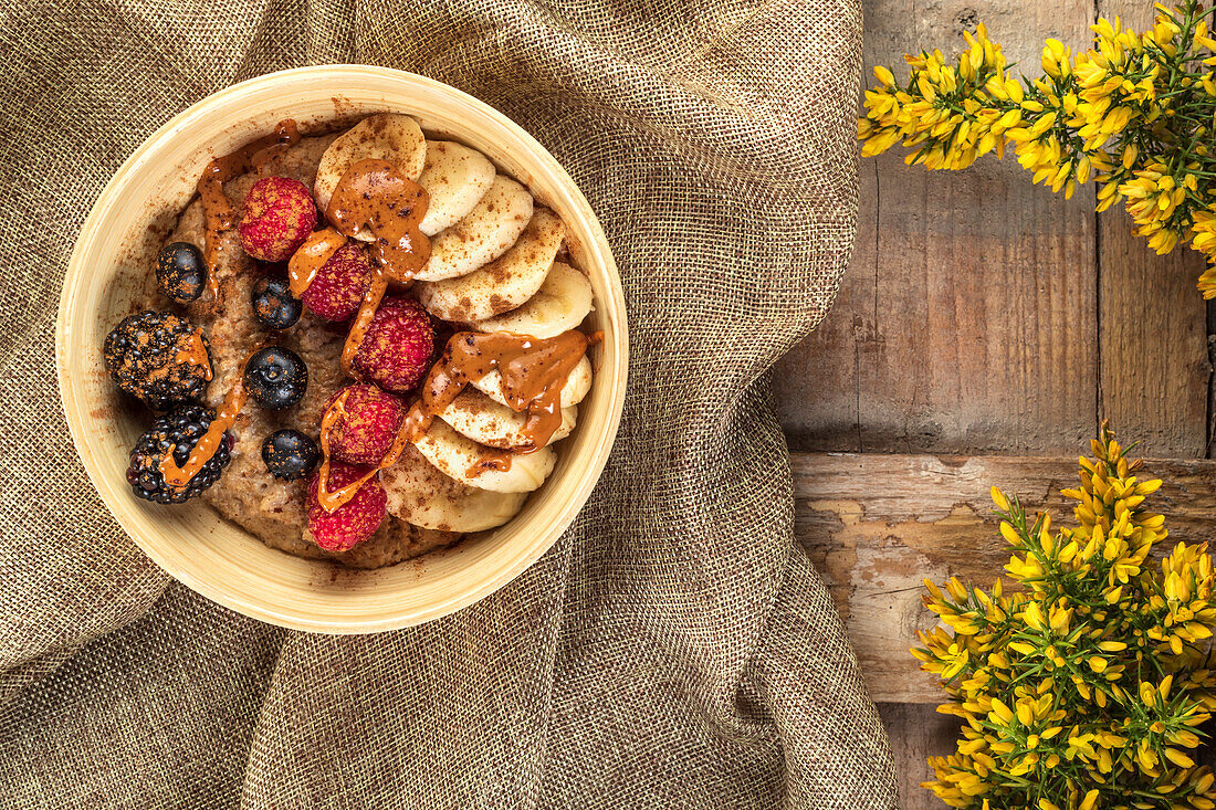 Overhead view of bowl with mix of ripe berries and banana slices covered with delicious caramel sauce on crumpled sackcloth