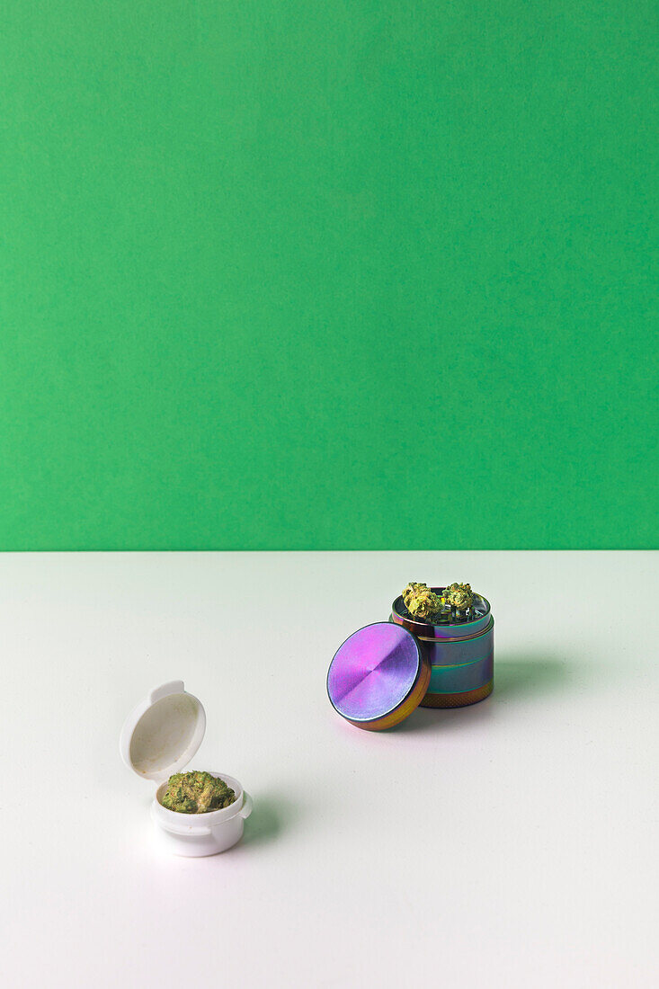 Dry cannabis plant in bowl on white surface with green background