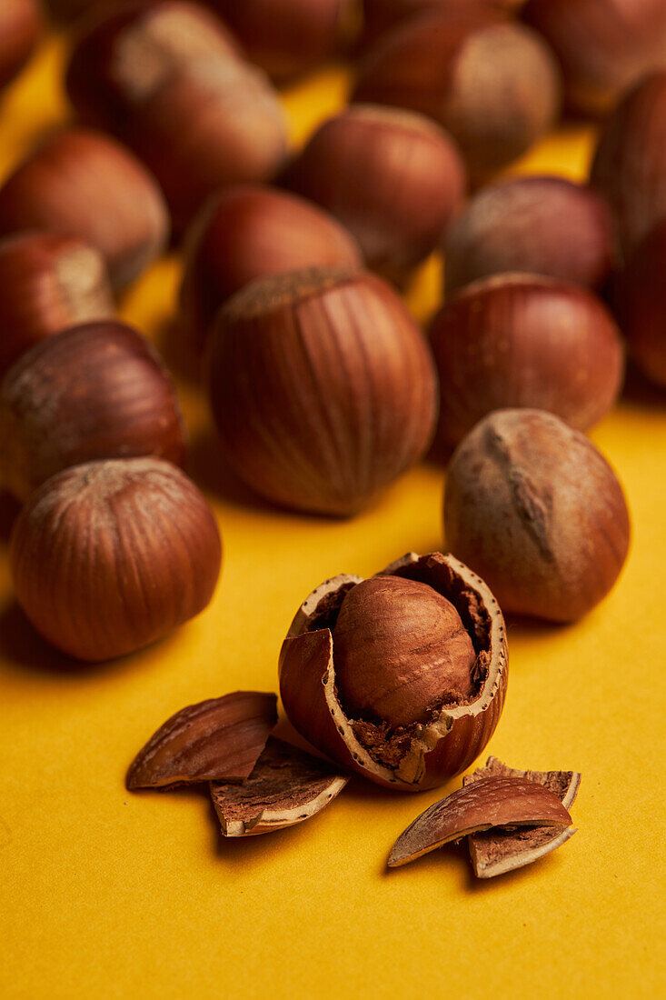 Closeup fresh hazelnut with cracked shell placed near bunch of ripe nuts on yellow background