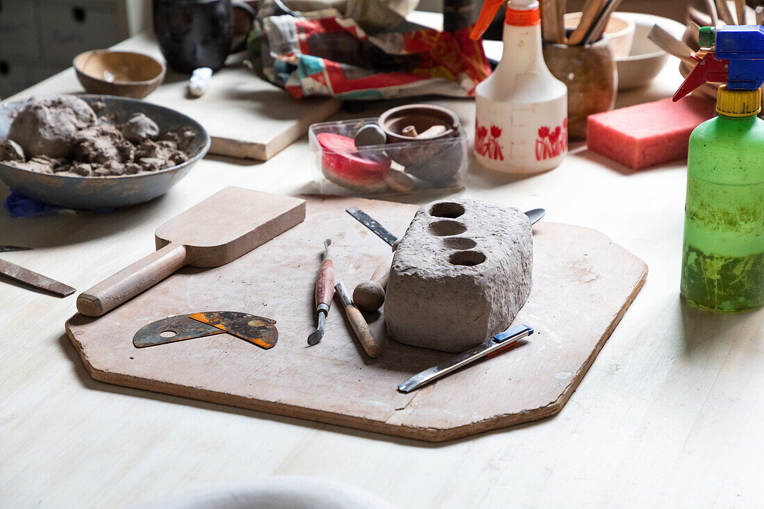 From above piece of clay placed on wooden board with various sculpting tools and metal pottery rib in workshop