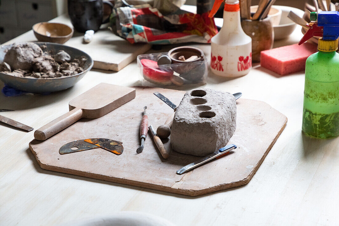 Von oben ein Stück Ton auf einem Holzbrett mit verschiedenen Bildhauerwerkzeugen und einer Metalltöpferrippe in einer Werkstatt