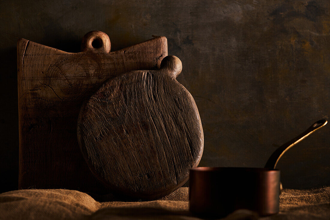 Handmade wooden chopping board of brown color placed on rustic table near pot in kitchen