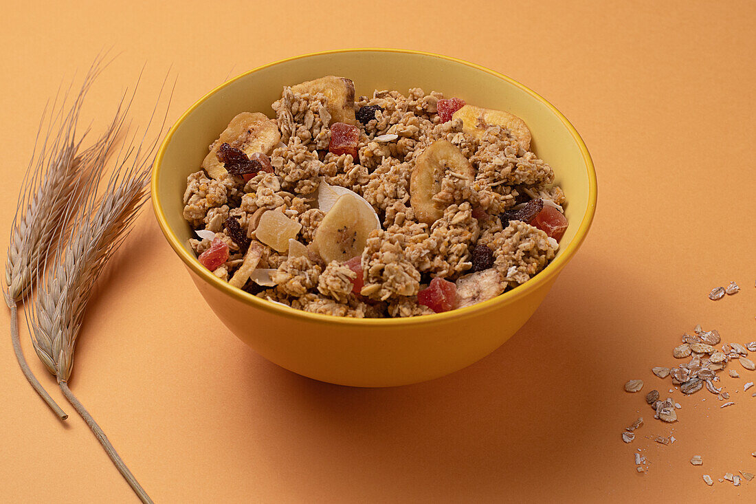 Von oben knuspriges Müsli mit getrockneten Früchten in Schale auf hellem Tisch mit braunem Hintergrund