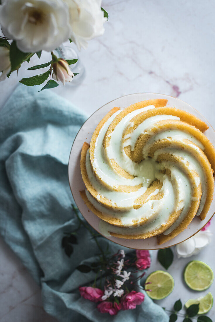 Top view of tasty lime sponge cake served on white plate near flowers and lime slices