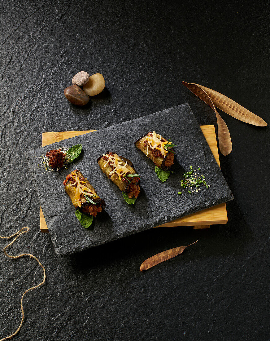From above of delicious baked eggplant rolls with minced meat mint and cheese served on dark board