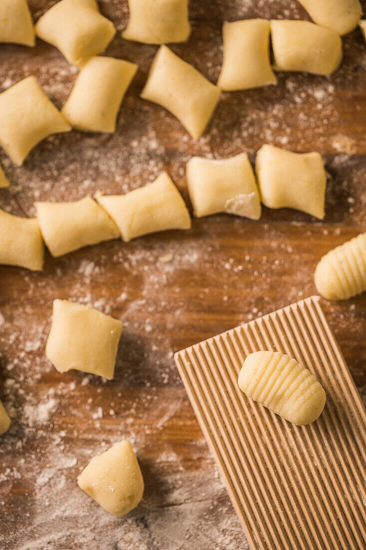 Top view of pieces of soft raw dough placed on wooden table covered with flour near ribber board during gnocchi preparation in the kitchen