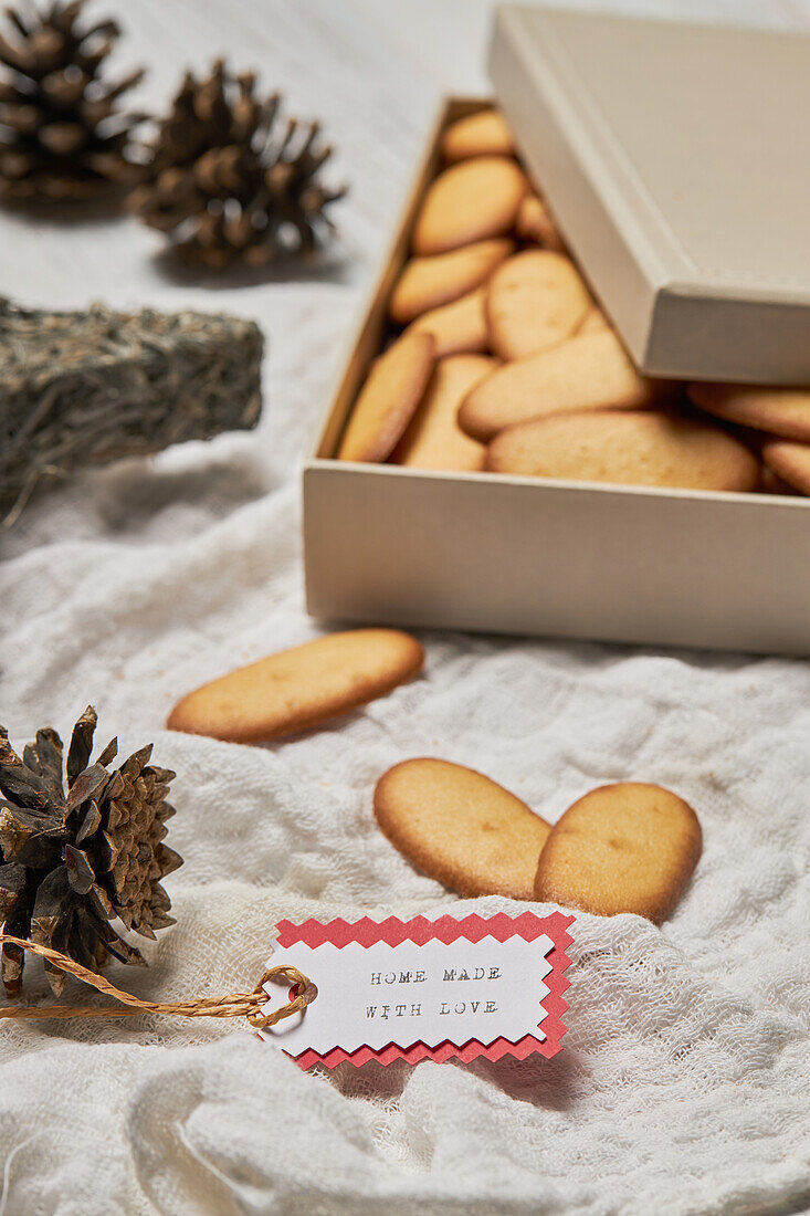 High angle of gift tag and cones placed on table with box full of homemade sweet Christmas biscuits
