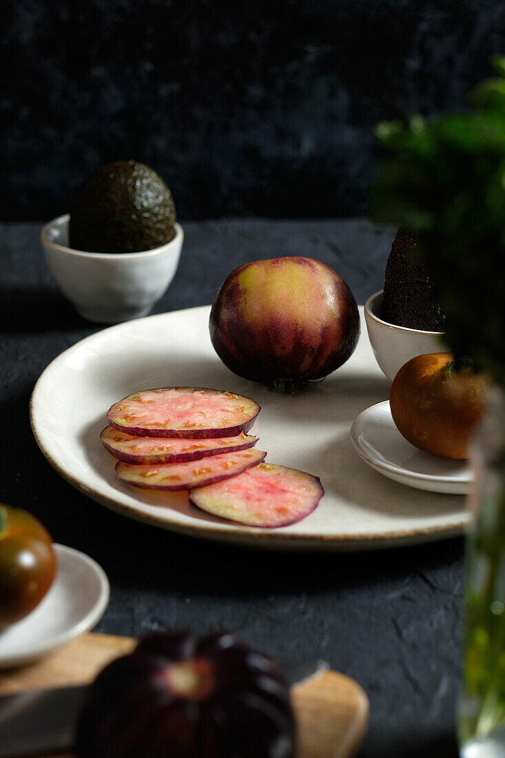 Von oben: Frische ganze und in Scheiben geschnittene schwarze Tomaten auf dem Tisch mit Avocado und grüner Minze bei der Zubereitung einer gesunden Mahlzeit