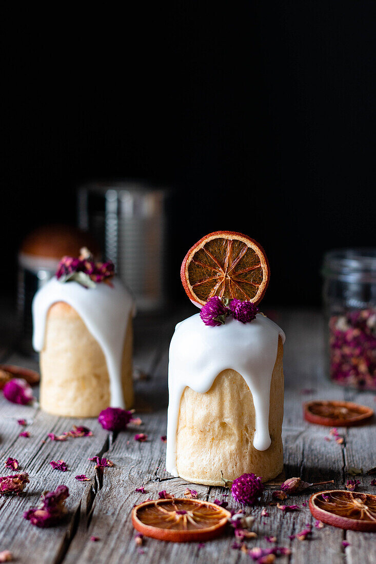 Mehrere köstliche hausgemachte Kulichs mit süßer Glasur übergossen und mit Stücken von getrockneten Orangen und Blumen auf einem Holztisch dekoriert