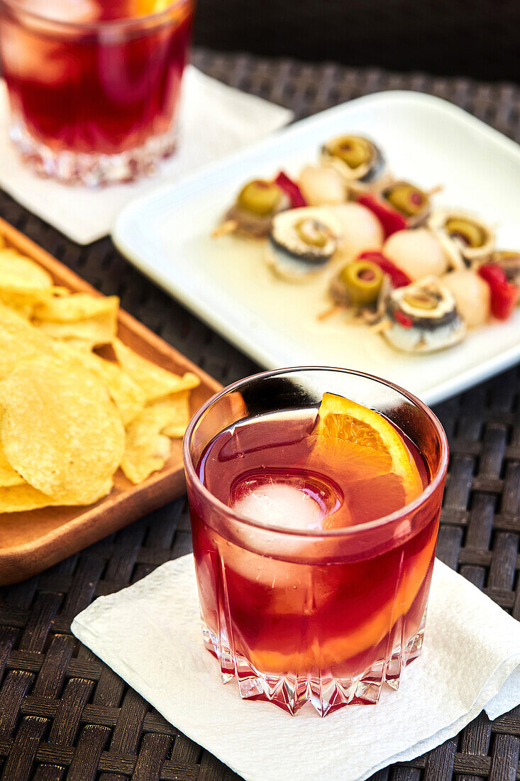 Von oben Glas mit kaltem, altmodischem Cocktail mit Eis und Orangenscheibe, serviert auf einem Tisch mit Vorspeisen