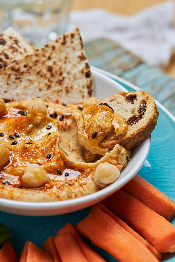 From above closeup bowl of yummy hummus with tortilla chips and croutons placed near slices of carrot during lunch