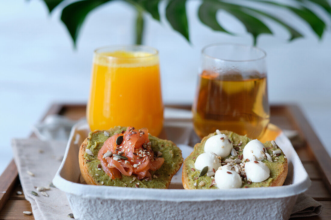 Gläser mit Saft und Kräutertee, serviert auf einem Holztisch mit verschiedenen gesunden Avocado-Toasts mit Käse und Lachs während des Frühstücks in einem Straßencafé