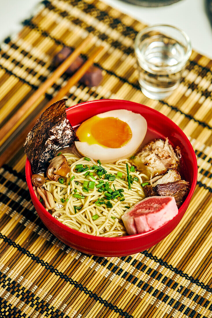 From above of appetizing ramen soup with meat and egg and noodles served in bowl on table near chopsticks and glass cup