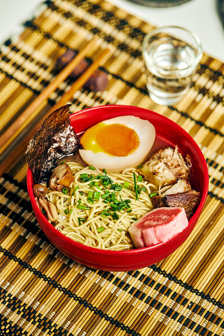 Von oben auf appetitliche Ramen-Suppe mit Fleisch und Ei und Nudeln, serviert in einer Schüssel auf einem Tisch neben Stäbchen und einer Glastasse