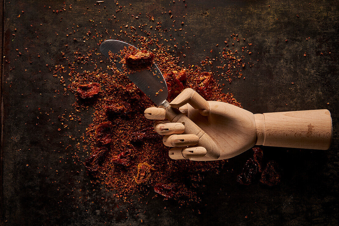 Top view composition with spilled aromatic natural ground sun dried tomatoes on dark table with knife in artificial wooden hand