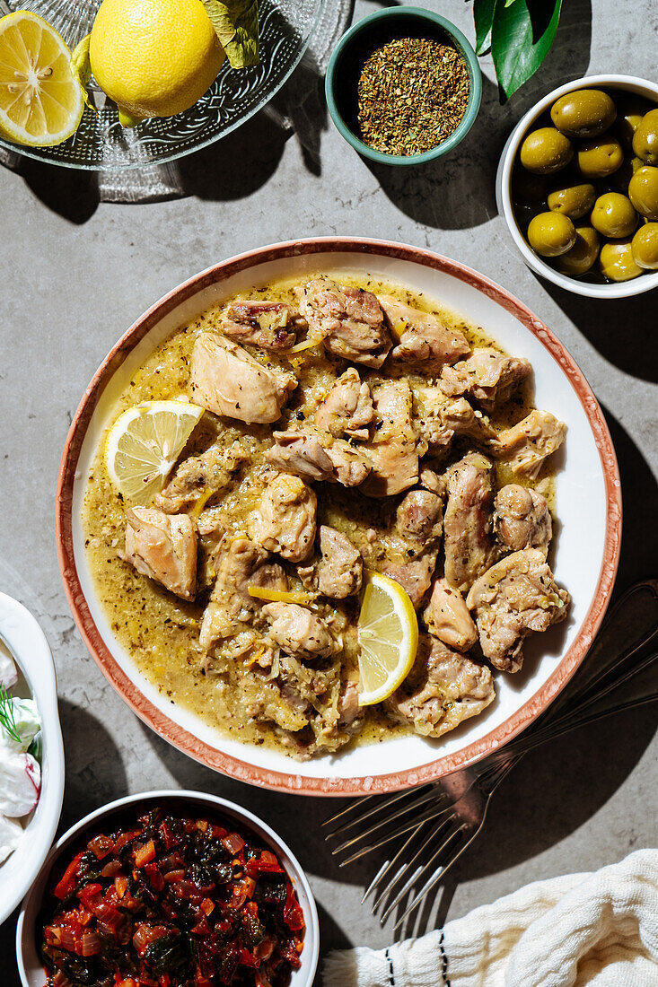 Draufsicht auf traditionellen griechischen Rindfleischeintopf mit Zitrone, serviert auf einem Tisch mit Oliven und Gewürzen in einer hellen Küche