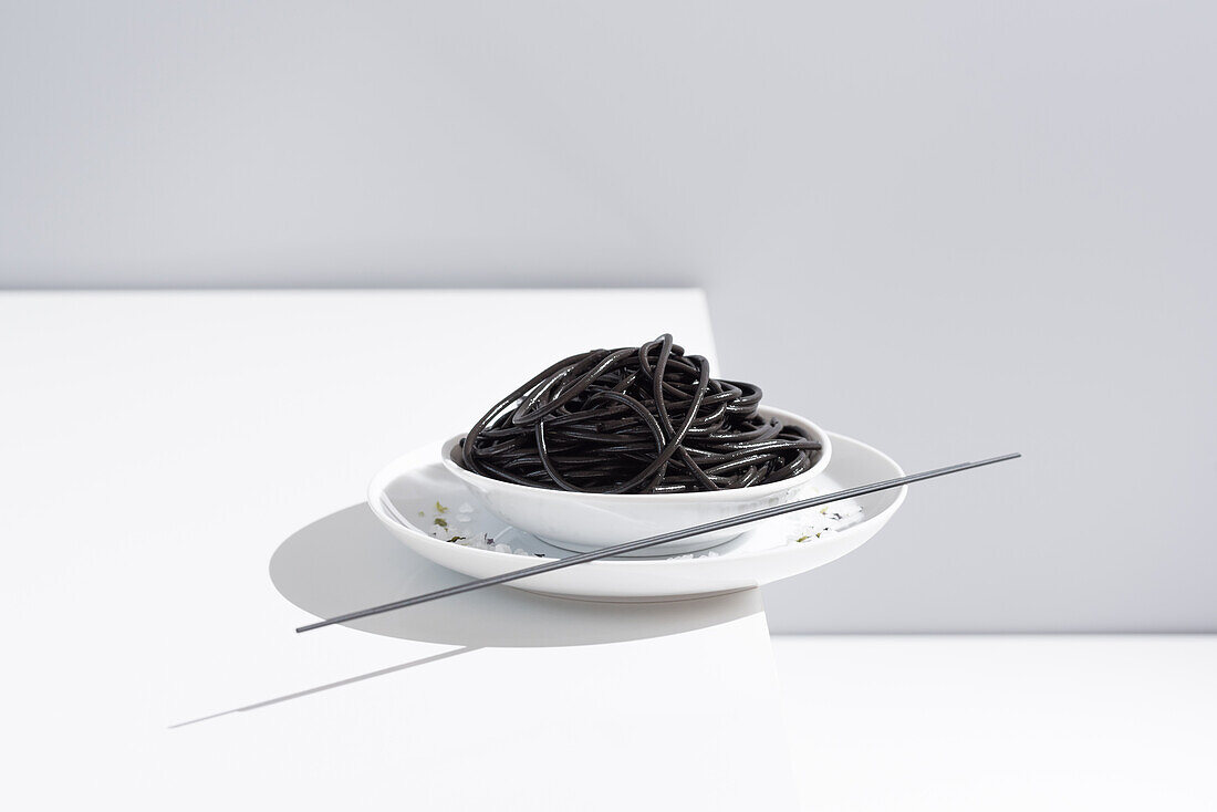 From above of ceramic bowl with delicious spaghetti with black squid ink with chopsticks on grey background