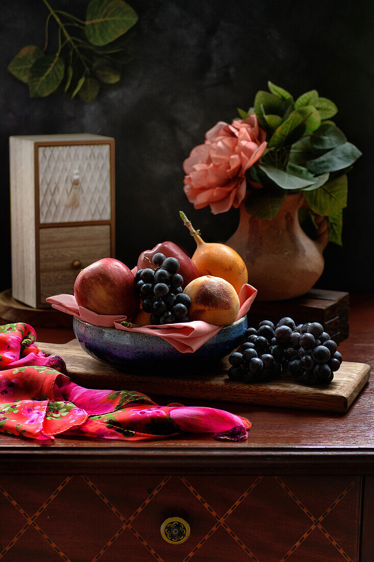 Fresh apples and peach with grapes and granadilla in bowl placed on table near red peony