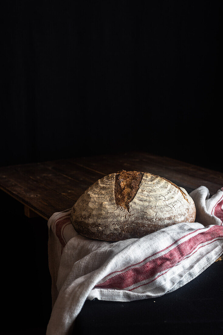 Homemade sourdough bread loaf with crispy crust on wooden rustic board on black background