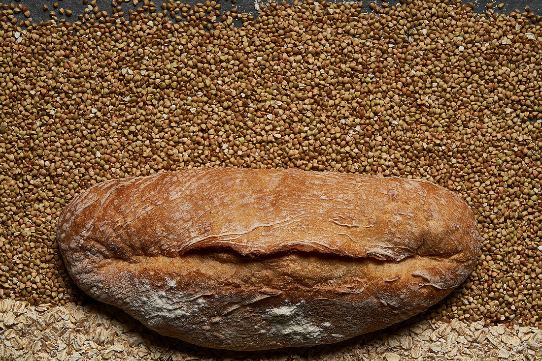 Top view full frame of fresh healthy brown baked bread placed on raw buckwheat and oat grains in light room