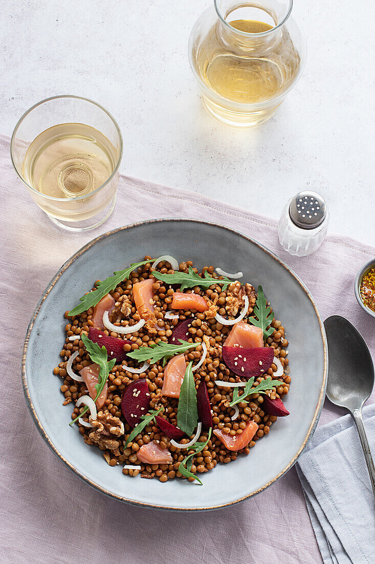 Nahaufnahme eines Lachs- und Linsensalats von oben auf einem Tisch mit rosa Tischtuch