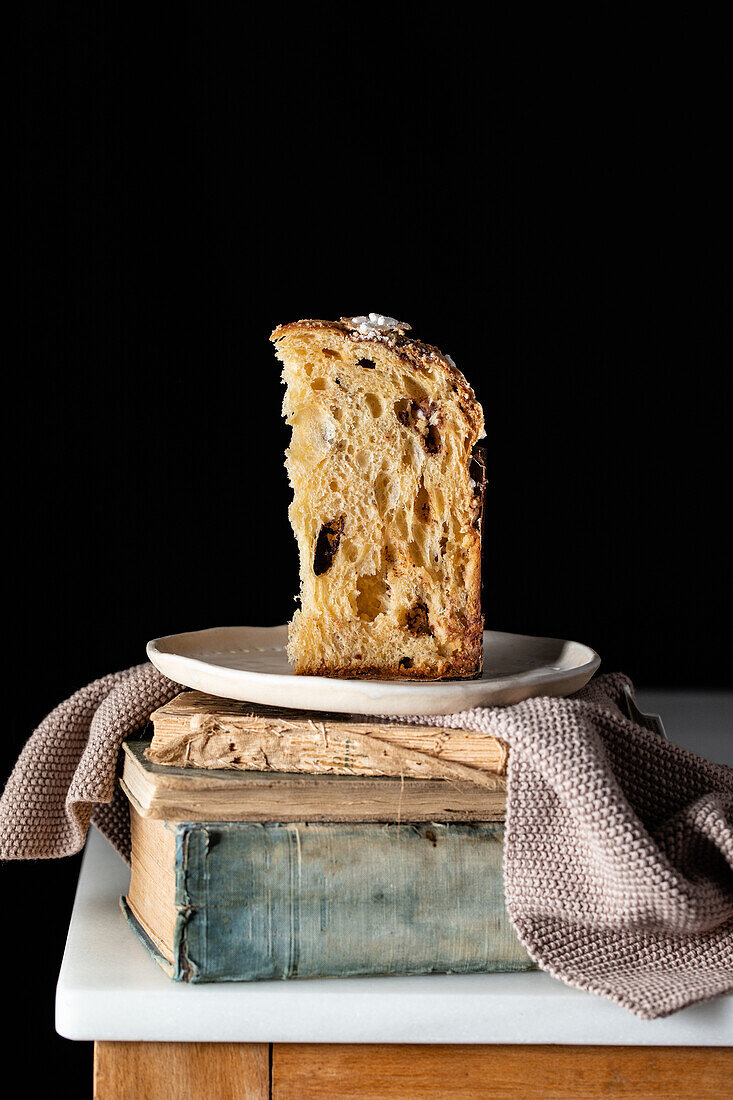 Delicious halve and whole of homemade panettones placed on aged books on wooden table against black background