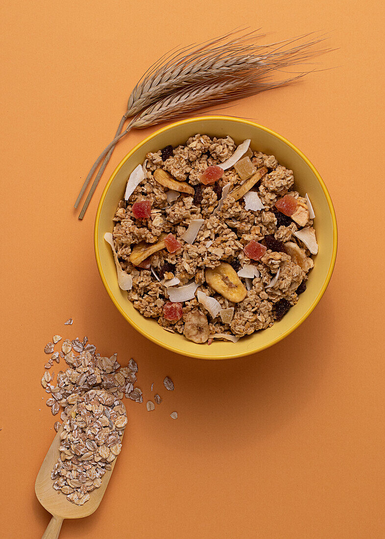 Von oben knuspriges Müsli mit getrockneten Früchten in Schale auf hellem Tisch mit braunem Hintergrund