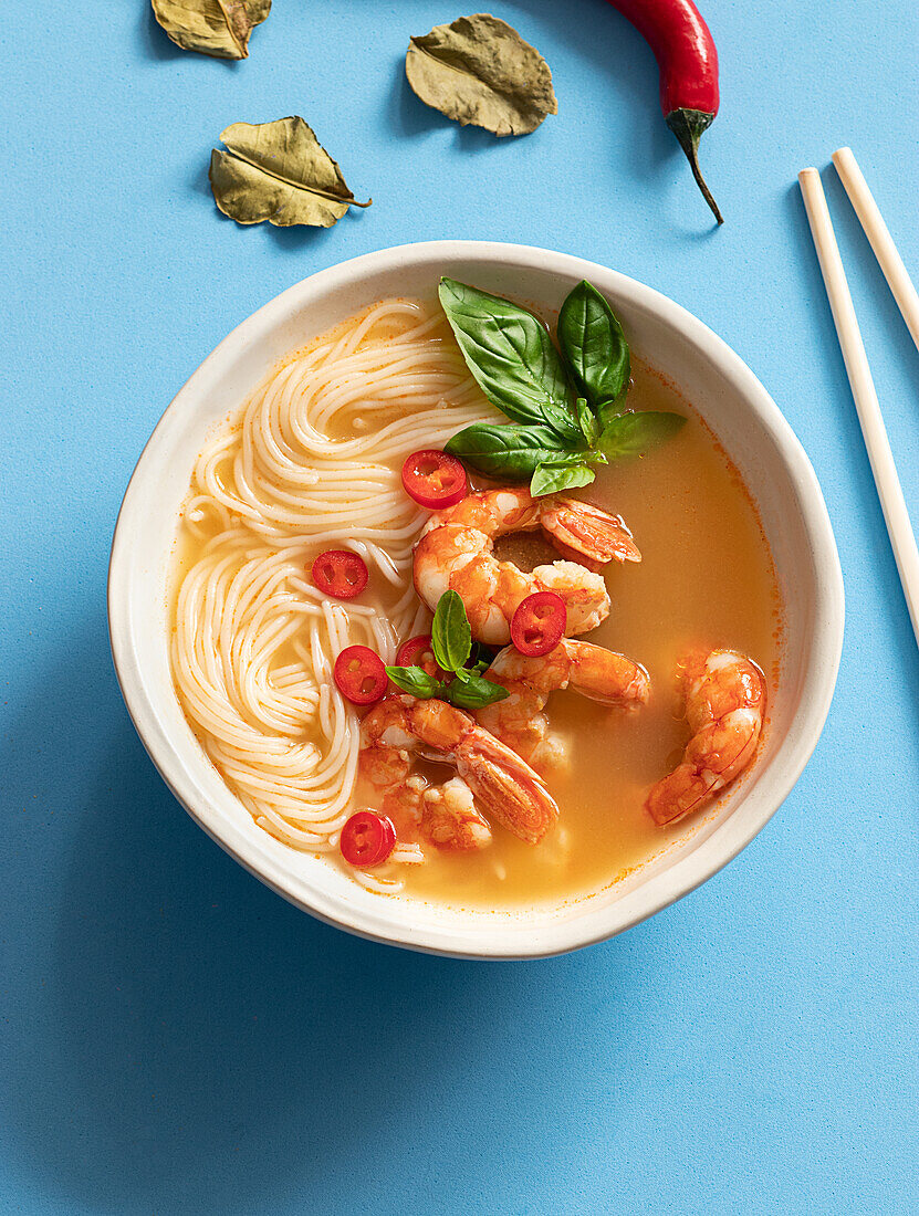 Tom-Yum-Suppe in Schüssel mit Stäbchen auf blauem Hintergrund