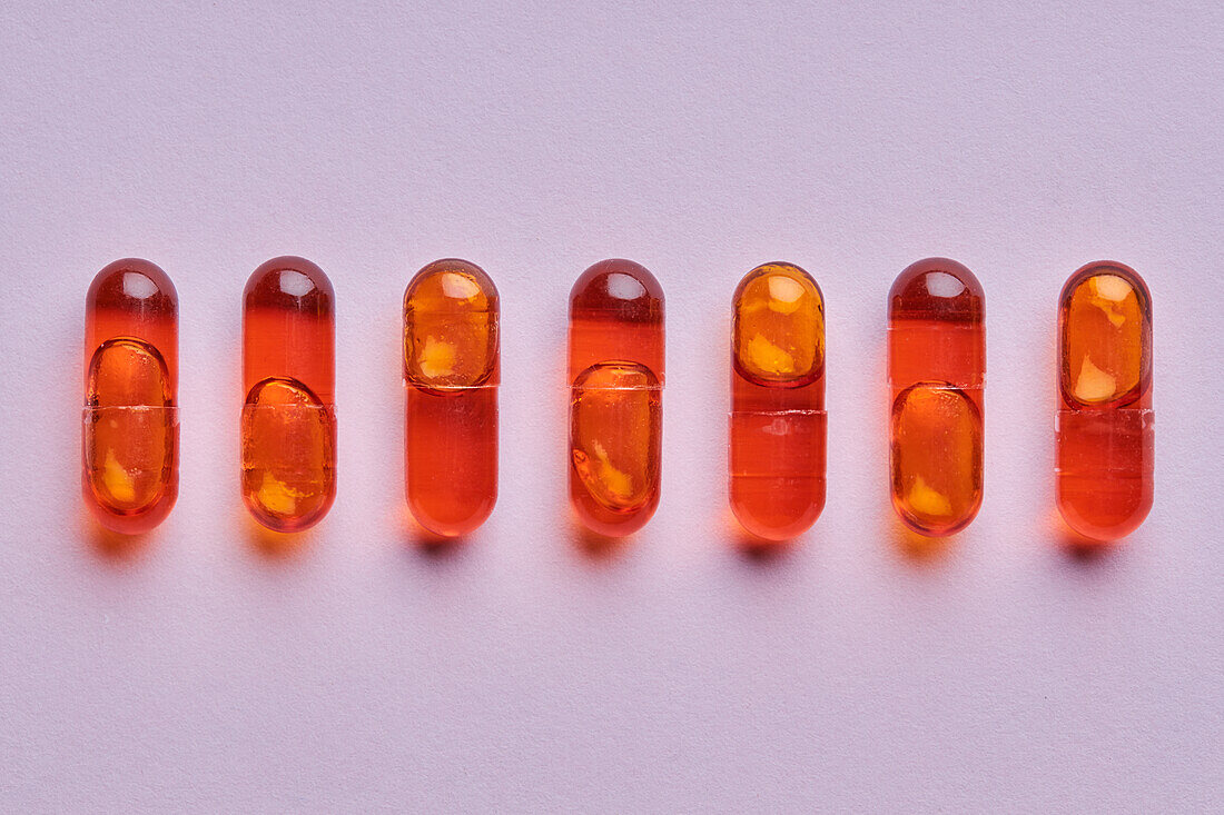 Top view composition of orange pills on pink background in light studio