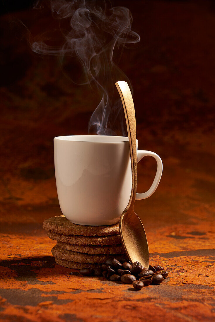 Ceramic mug of hot aromatic drink and spoon place on surface near pile of fresh baked oatmeal cookies