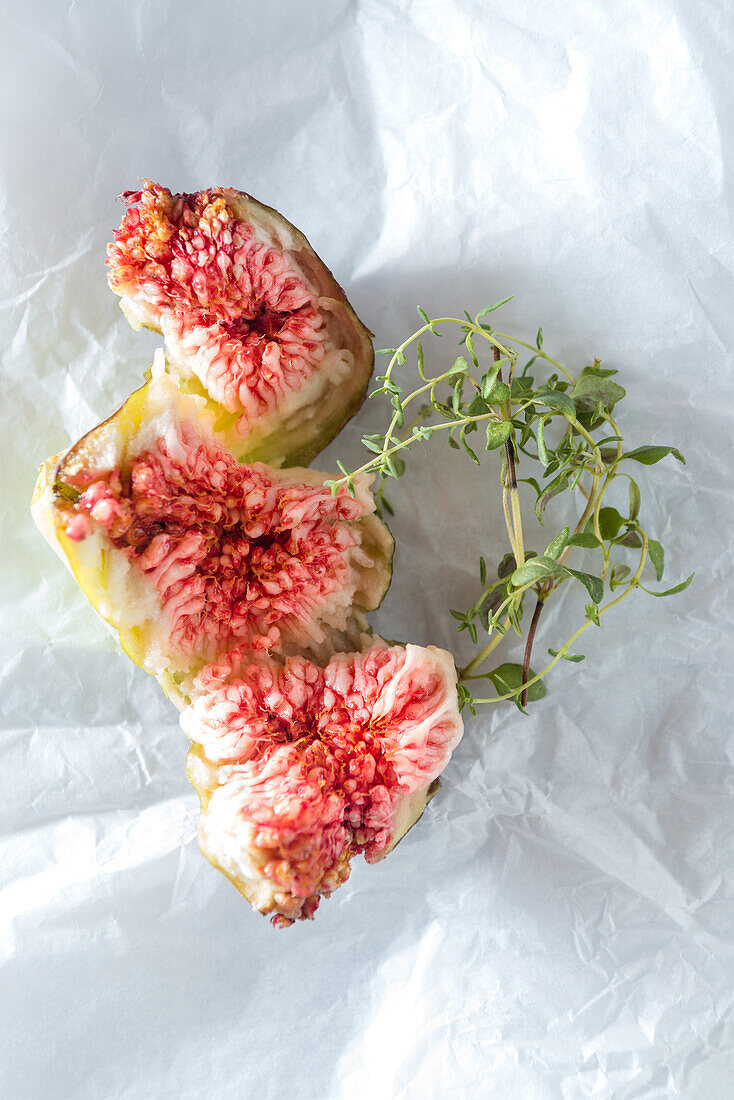 Top view of tasty fresh fig pieces with juicy pulp near aromatic thyme sprigs on crumpled surface