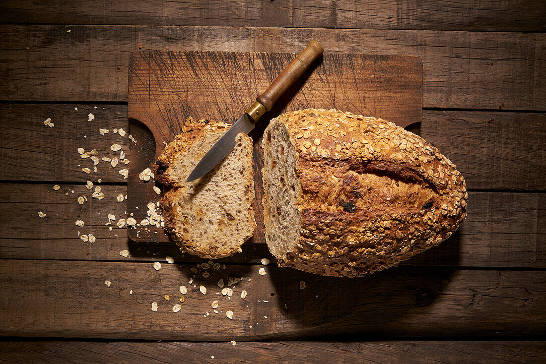 Top view of delicious freshly baked sourdough bread loaf with sliced piece and knife placed on cutting board on table