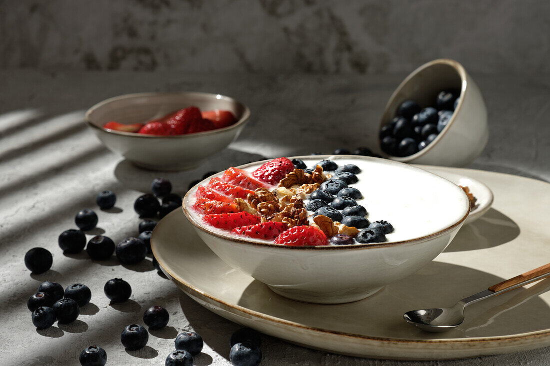 Draufsicht auf eine leckere gesunde Frühstücksschüssel mit weißem Joghurt und frischen Erdbeeren und Blaubeeren mit Müsli