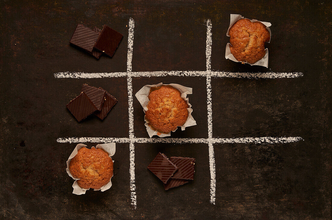 Draufsicht auf ein essbares Tic-Tac-Toe-Spiel mit gebackenen Muffins und süßer Schokolade, die ein Viereck darstellen, auf schwarzem Hintergrund