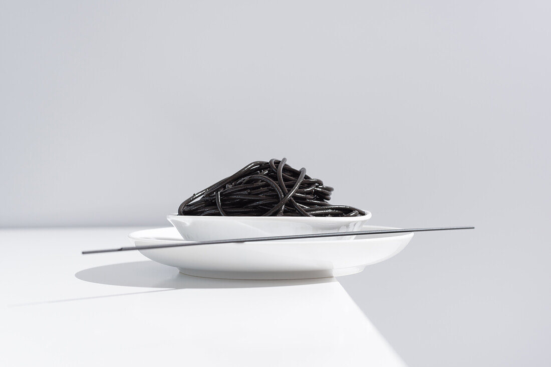 Von oben auf Keramikschale mit leckeren Spaghetti mit schwarzer Tintenfischtinte mit Stäbchen auf grauem Hintergrund