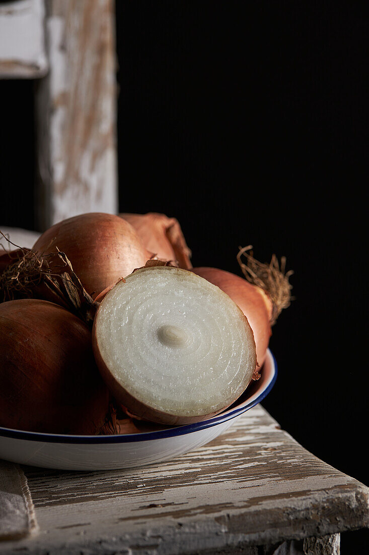 Closeup halved and whole unpeeled onions placed in bowl on shabby chair on black background