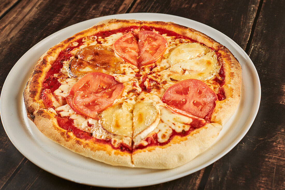 Aufgeschnittene Pizza mit natürlichen Tomatenscheiben und Ziegenkäse, serviert auf einem Teller auf einem Holztisch in einer Pizzeria